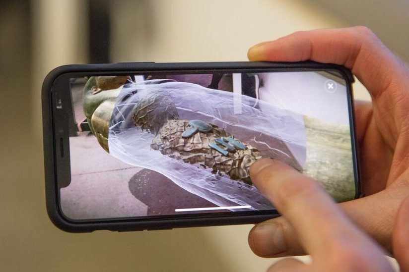 A hand holding a phone displaying an AR app for exploring ancient artefacts.