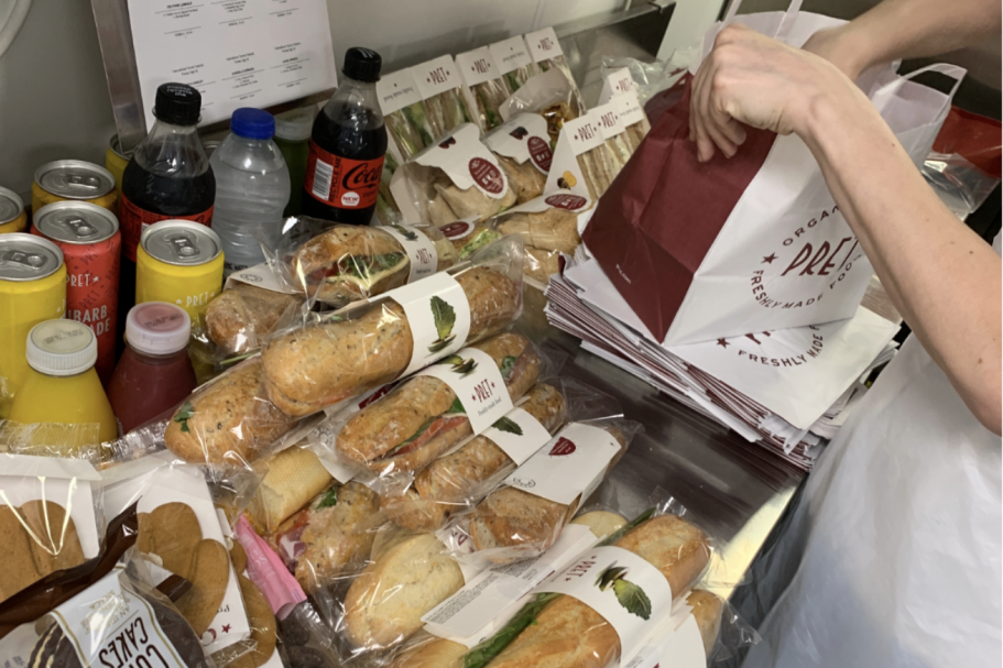 A selection of assorted sandwiches and drinks on a table, with someone packing a bag.